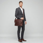 Chris Louis Bethlehem brown leather messenger bag with double lock closure and adjustable strap, worn by a woman in a cafe.