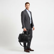 Chris Louis black leather briefcase with detachable shoulder strap, held by a woman in a white shirt and grey trousers.
