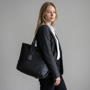 Chris Louis black pebbled leather tote bag with shoulder strap and leather tag, worn by a woman in a suit.