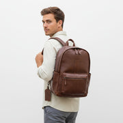 Chris Louis warm brown genuine leather backpack with front zip pocket, side pockets, and detachable luggage tag.