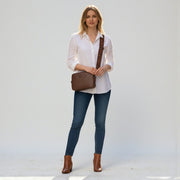Chris Louis Moolicious brown full grain leather sling bag with webbed strap, worn by a woman on a cobblestone street.