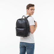 Chris Louis navy leather backpack with front zip pocket and side pockets, worn by a woman in jeans and a white t-shirt.