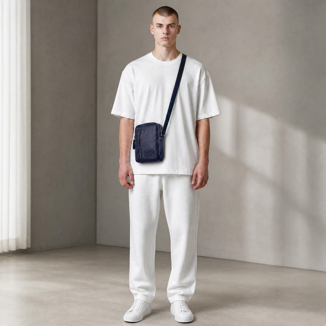Chris Louis navy blue leather cross-body bag with front zipper pocket and adjustable strap, worn by a male model.