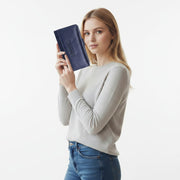 Chris Louis navy blue leather trifold wallet with snap closure and zippered coin pocket, held by a woman in jeans and a grey sweater.