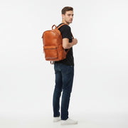 Chris Louis genuine leather backpack in orange, featuring multiple compartments and adjustable straps, worn by a woman on a cobblestone street.