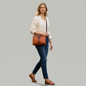 Chris Louis Santorini tan leather crossbody bag with front flap and metal hardware, worn by a woman walking on a cobblestone street.