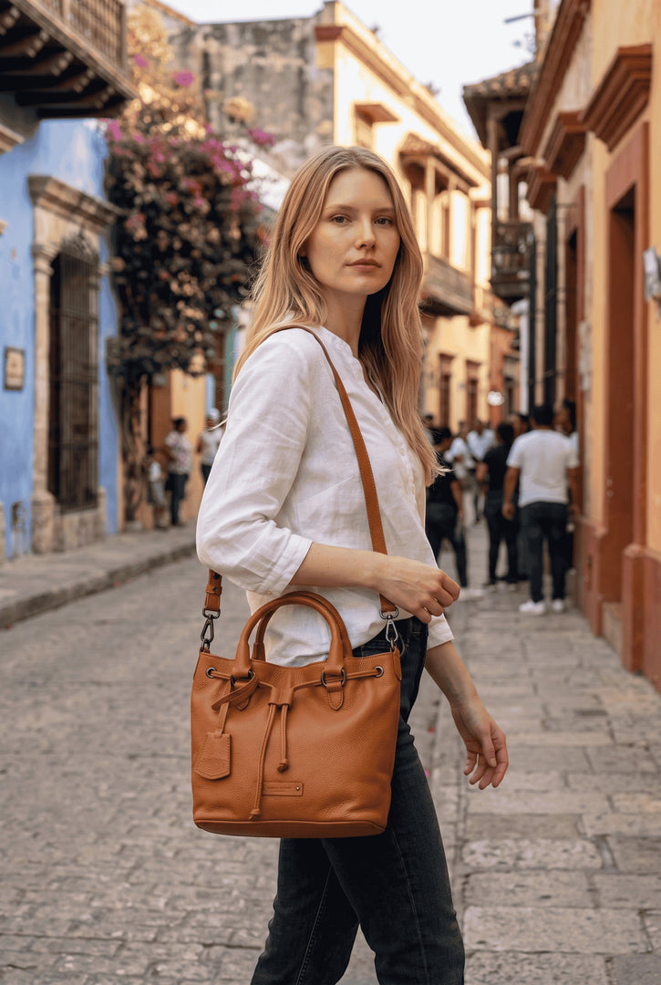 A woman wearing a Chris Louis tan full grain leather satchel bag with drawstring and crossbody strap on a city street.