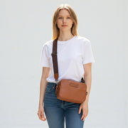 Chris Louis Moolicious sling bag in tan full grain leather with signature webbed strap, worn by a woman.